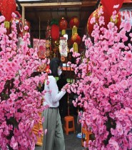 امرأة تمشي وسط الورود بينما يتسوق الناس لشراء الحلي والأطعمة الصينية في جاكرتا، قبل رأس السنة الصينية الجديدة في 22 يناير - ا ف ب