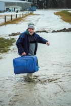 رجل يسير في مياه الفيضانات حاملا حقيبة كبيرة بالقرب من بلدة أشبورتون في كانتربري حيث أعلنت السلطات النيوزيلندية حالة الطوارئ بعد تعرض المنطقة لهطول أمطار غزيرة. ا ف ب