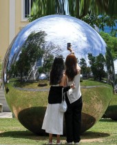 فتاتان تقفان لالتقاط صور أمام دائرة فنية عبارة عن كرة عاكسة من الفولاذ المقاوم للصدأ في حديقة عامة في سنغافورة  (ا ف ب)