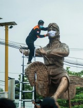 عامل يضع قناعًا جراحيًا وهميًا على أحد التماثيل القديمة في يوجياكارتا، لتشجيع السكان على ارتداء الماسك مع ارتفاع معدلات الإصابة في إندونيسيا.ا ف ب