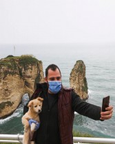 رجل يرتدي كمامة ويلتقط صورة سيلفي وهو يحمل كلبه أمام صخرة الحمام في بيروت ، لبنان.  (رويترز)