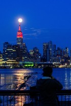 القمر يضيء خلف مبنى إمباير ستيت بينما يضيء المبنى باللون الأحمر للتضامن مع المصابين بفيروس كورونا في حي مانهاتن بمدينة نيويورك. رويترز