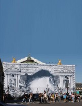 أشخاص يسيرون أمام عمل فني للفنان الفرنسي الشهير جيه آر على واجهة دار الأوبرا «أوبرا غارنييه» أثناء تجديدها في باريس (ا ف ب)