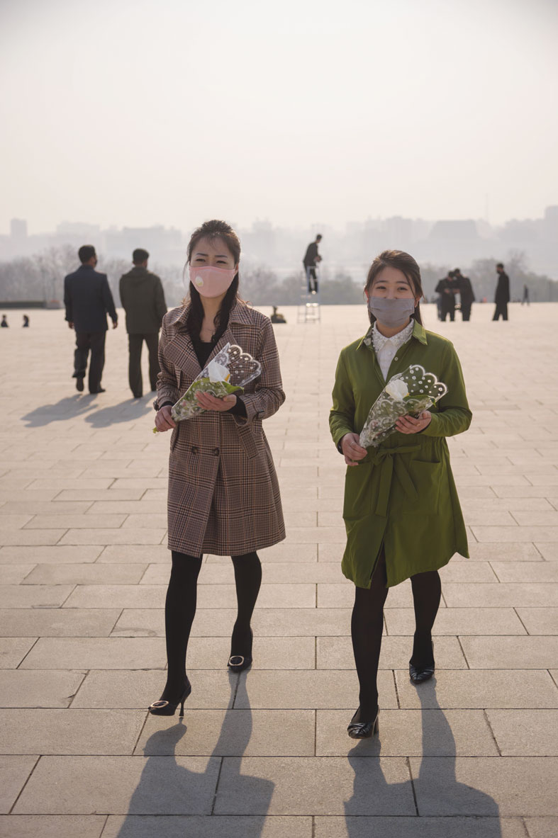 فتاتان ترتديان أقنعة للوجه وتستعدان لوضع الزهور أمام تماثيل الزعيم الكوري الشمالي الراحل كيم إيل سونغ بمناسبة عيد الميلاد الـ  108 للزعيم الكوري الشمالي الراحل، المعروف باسم يوم الشمس ، في بيونغ يانغ. (ا ف ب)