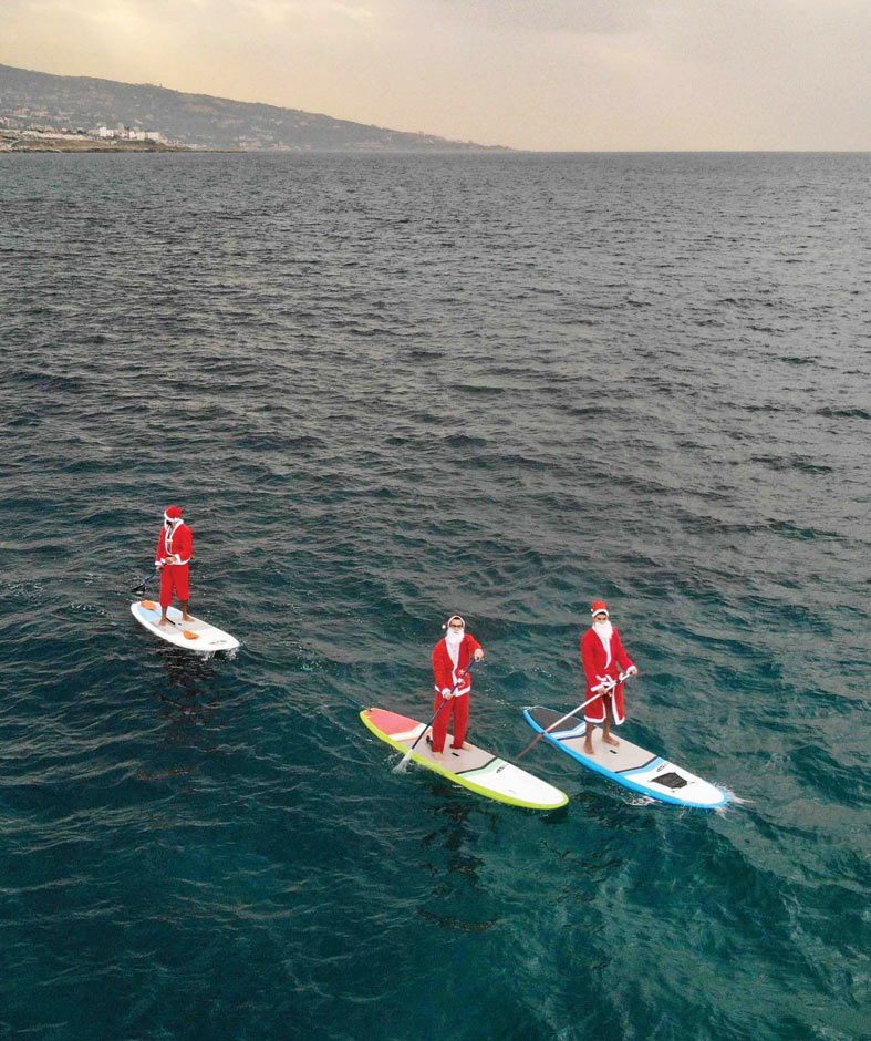 لبنانيون يرتدون ملابس سانتا كلوز ويركبون مجاديف في مدينة البترون الساحلية شمال لبنان. (ا ف ب)